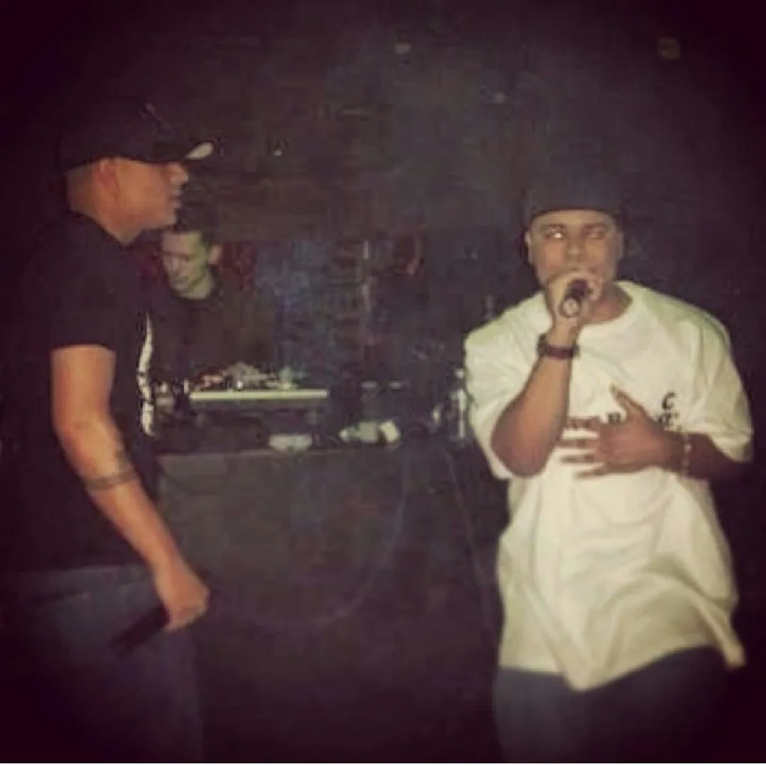 Andre Ramone performing on a dark stage with a microphone while another member of OC Uprise looks on
